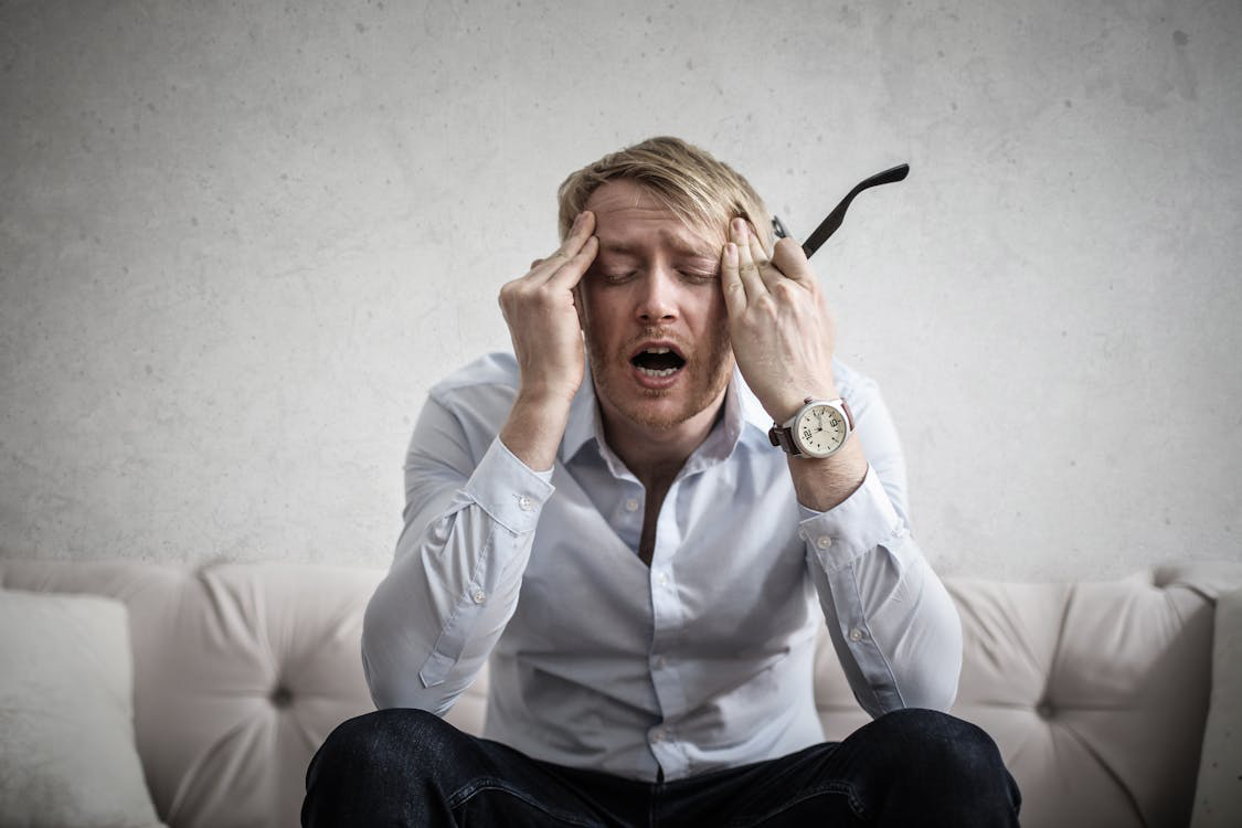 A Man on a Couch with B12 Deficiency Massages His Head in Obvious Distress