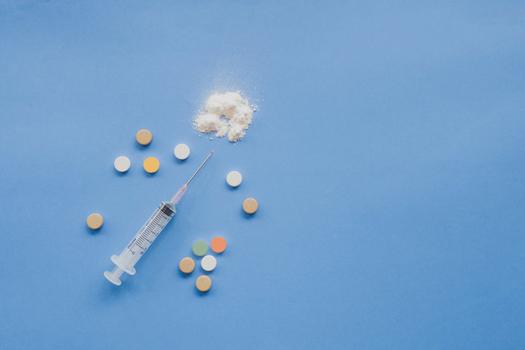 An Empty Syringe Surrounded by Vitamin B12 Pills, Whole and Crushed