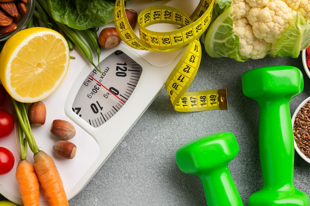 Flat lay composition of a digital scale and colorful dumbbells on a healthy green background.