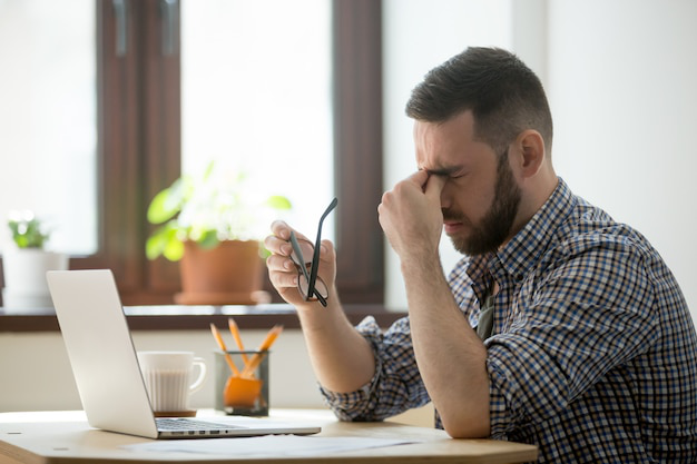 Man looking stressed and tired, rubbing his nose bridge with eyes closed, depicting symptoms of fatigue.