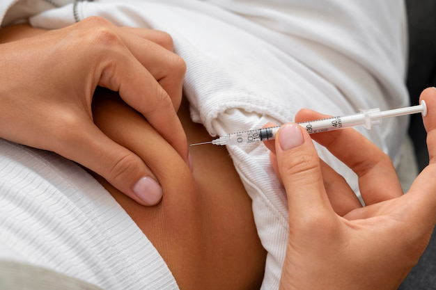 Close-up image of a woman's hand administering a Semaglutide injection into her stomach area.