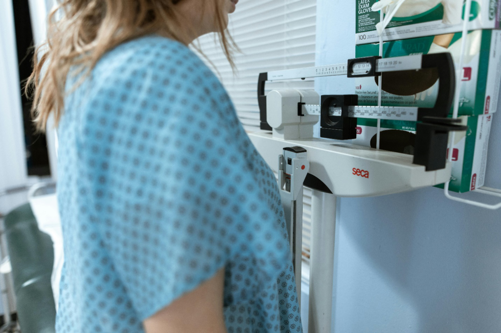 A person in a hospital gown stands on a weighing scale in a clinic setting