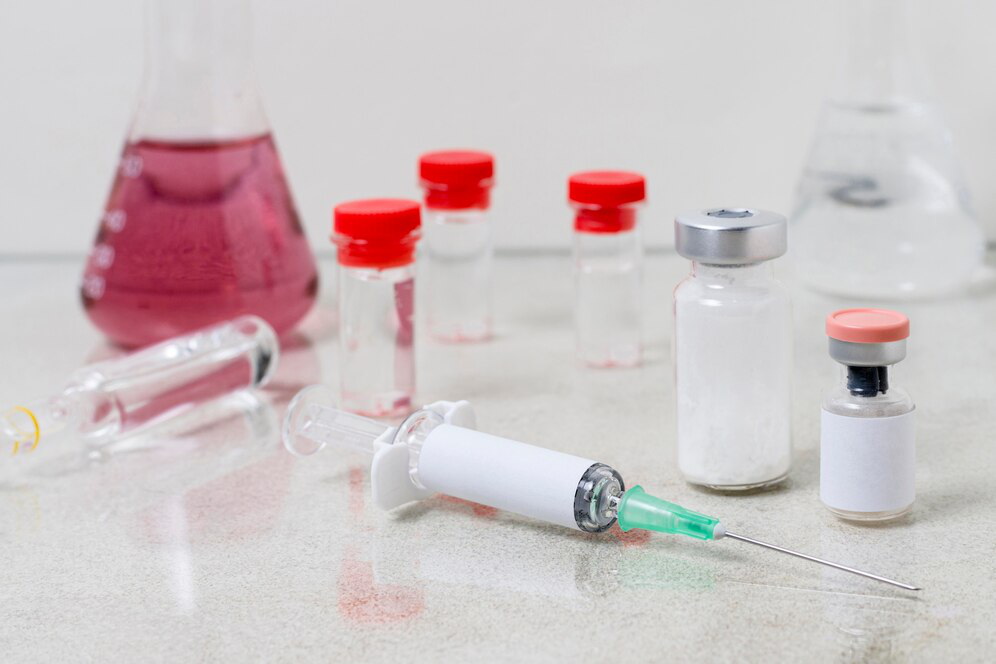 Vials of various shapes and sizes sit by a syringe with a needle and beakers, showing the process of putting together injectable weight loss solutions.