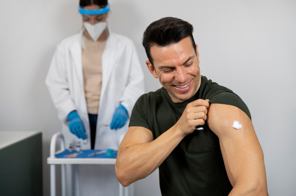 A man in a black t-shirt smiles while looking at his arm with a bit of cotton and bandaid, showcasing how painless getting lipotropic injections can be