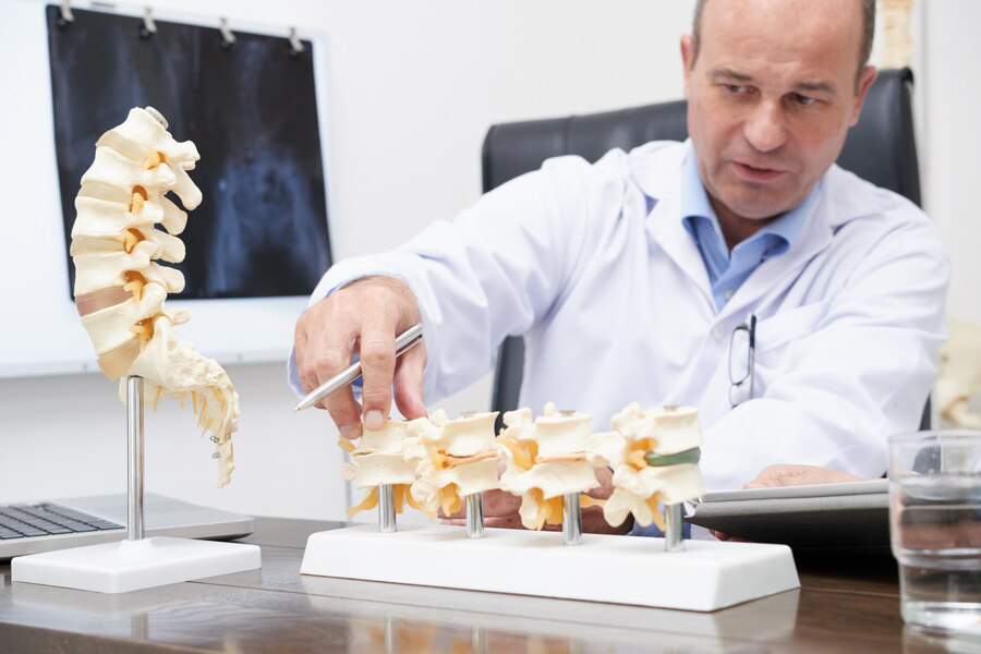 A person in a white lab coat looks at models of bones of the spine with an x-ray behind him, signifying how Sermorelin injections can aid in bone density and strength