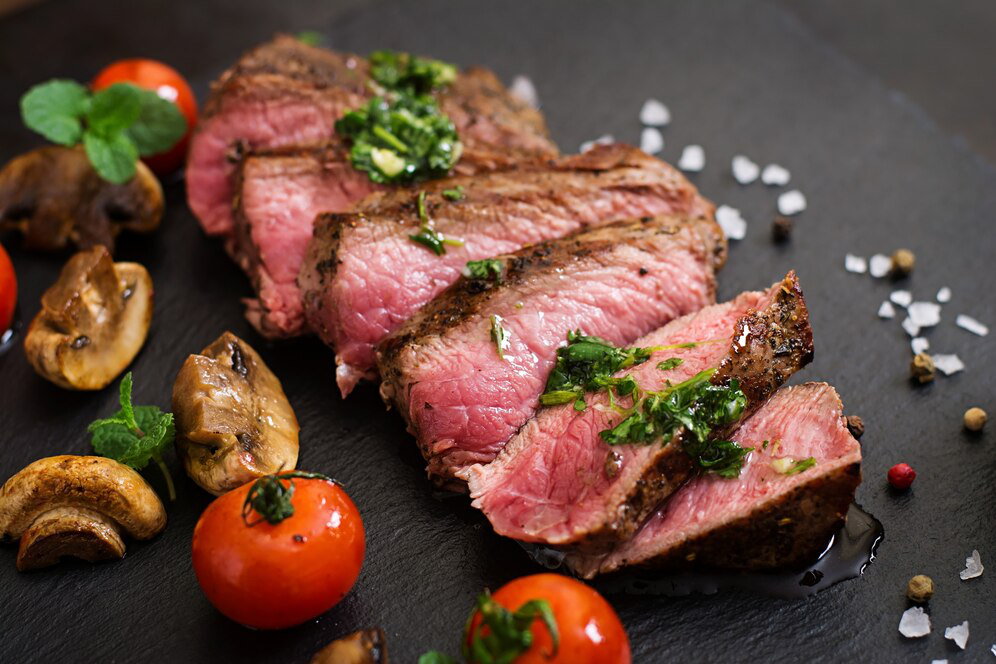 Sliced steaks on a black surface with cherry tomatoes and sliced mushrooms, a high-protein meal for weight loss