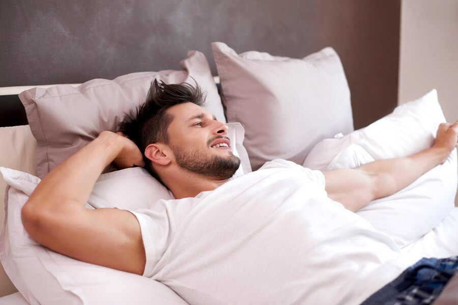 A man in a white t-shirt lies in bed