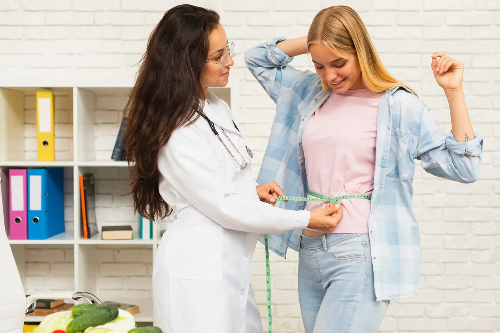 A person in a lab coat and stethoscope measures a woman’s waist