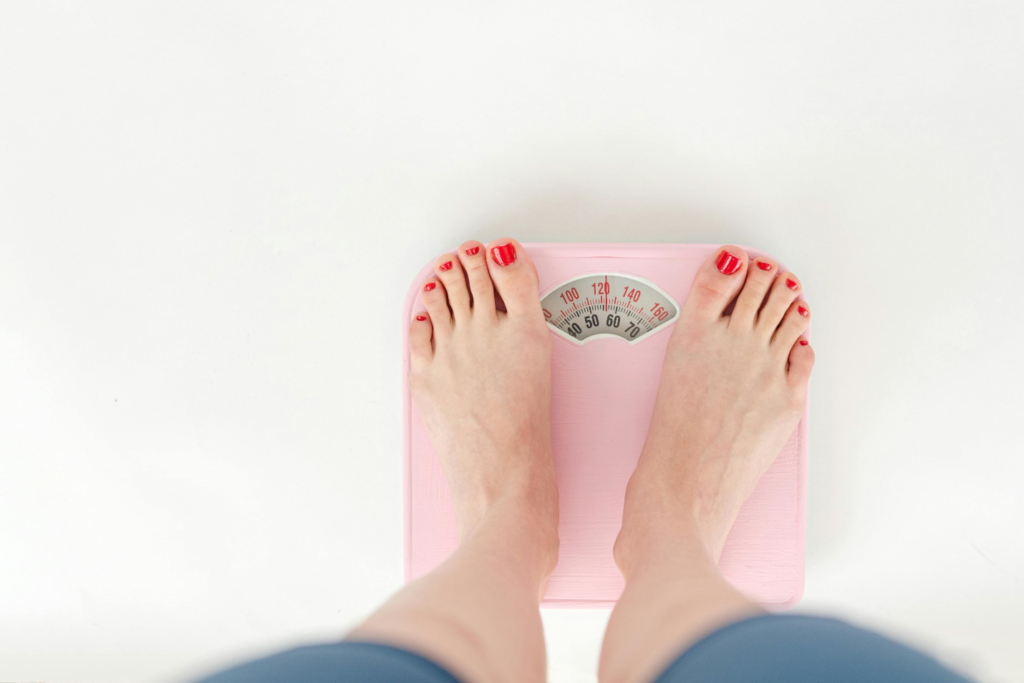 A person’s feet with red nail polish seen standing on a light pink weighing scale showing 122 pounds