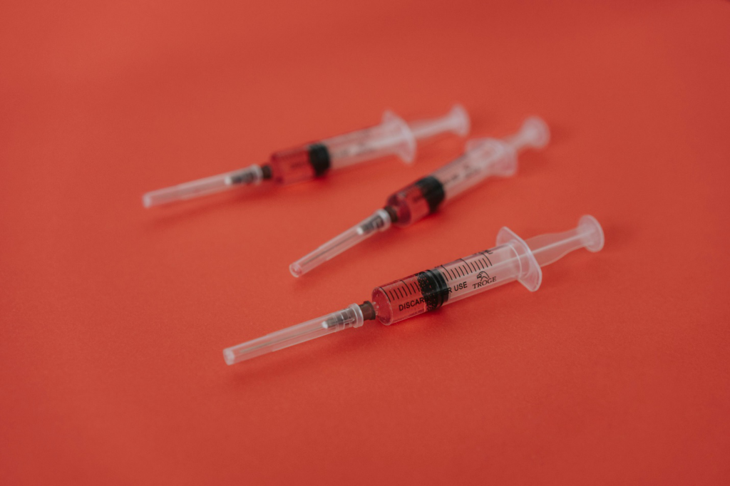 Three red injections loaded with a reddish liquid sit on a red surface