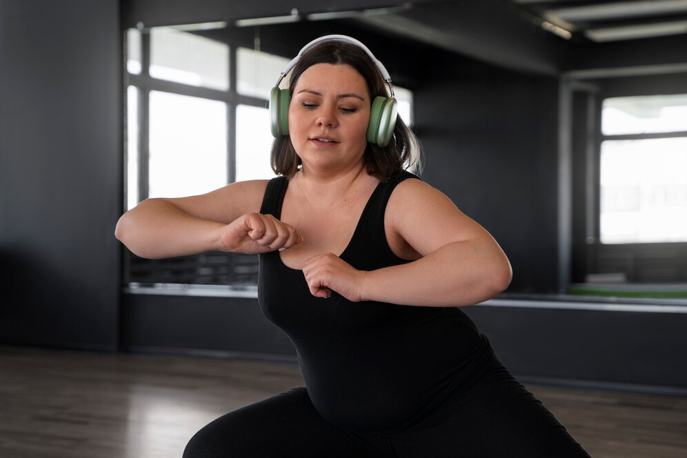  A woman in a black tank wearing silver headphones works out by a mirror