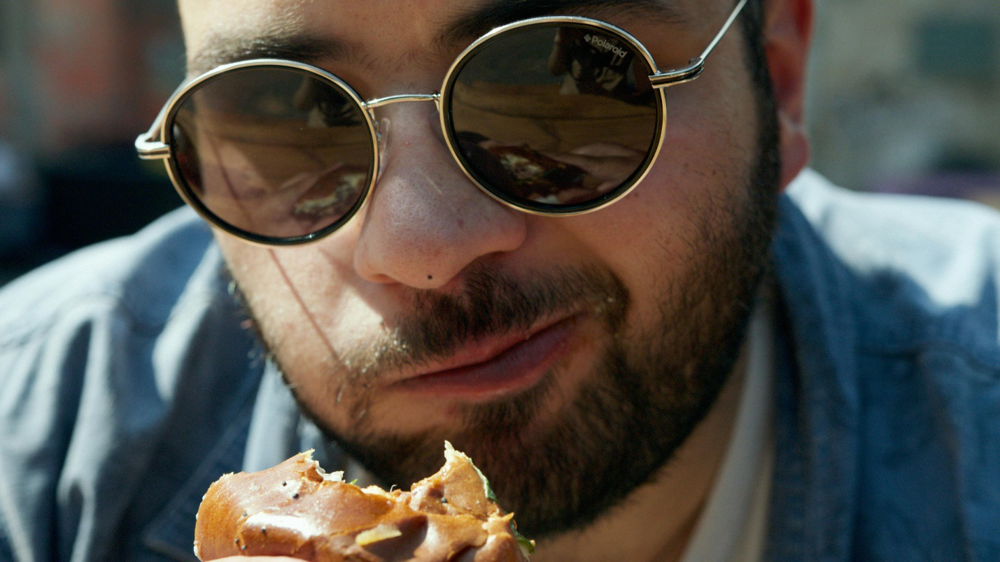 A close-up of a man in sunglasses holding a burger near his face