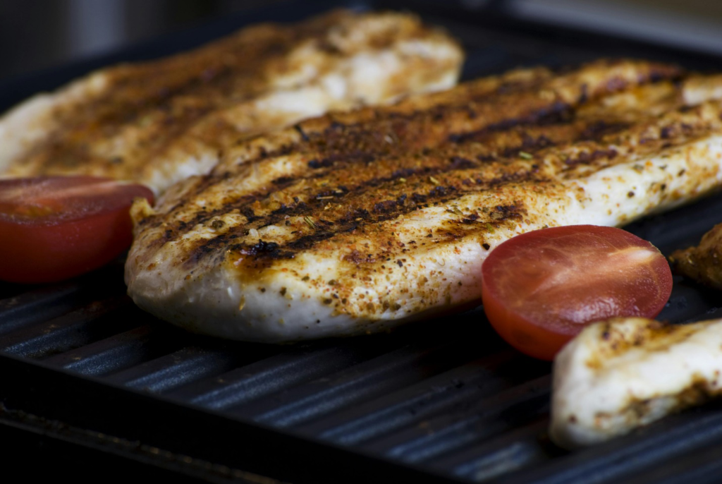 Filets of grilled chicken breasts on a skillet with chopped tomatoes highlighting the high-protein diet that’s recommended in weight loss programs