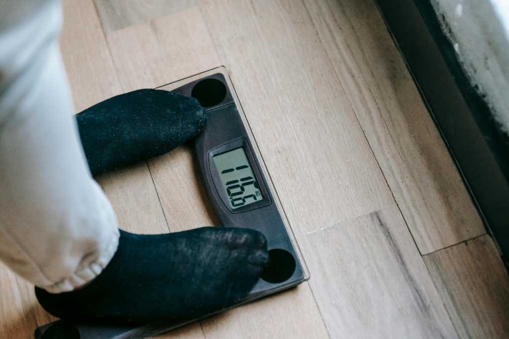 A person’s feet in black socks standing on a digital weighing scale reading 116.6kg