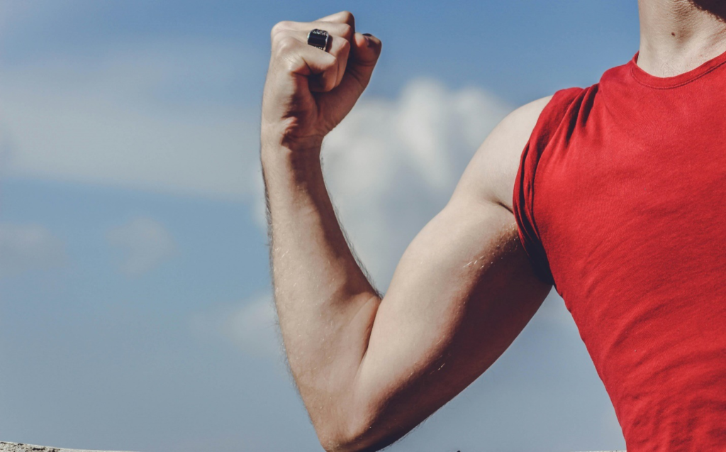 A close-up of a person’s arm while flexing muscles in a red t-shirt