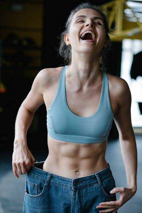 Woman celebrating weight loss success by showing loose pants after achieving her fitness goals.