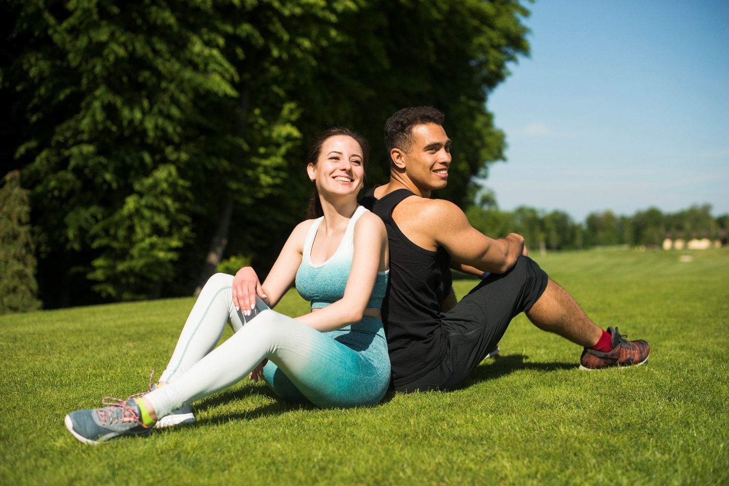  Smiling couple sitting on the grass after an active workout, showcasing a healthy lifestyle post-weight loss treatment.