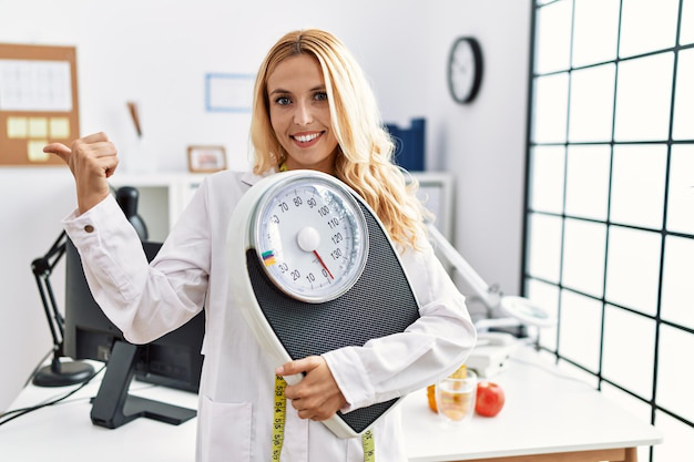 A weight loss specialist holding a scale and giving a thumbs-up.