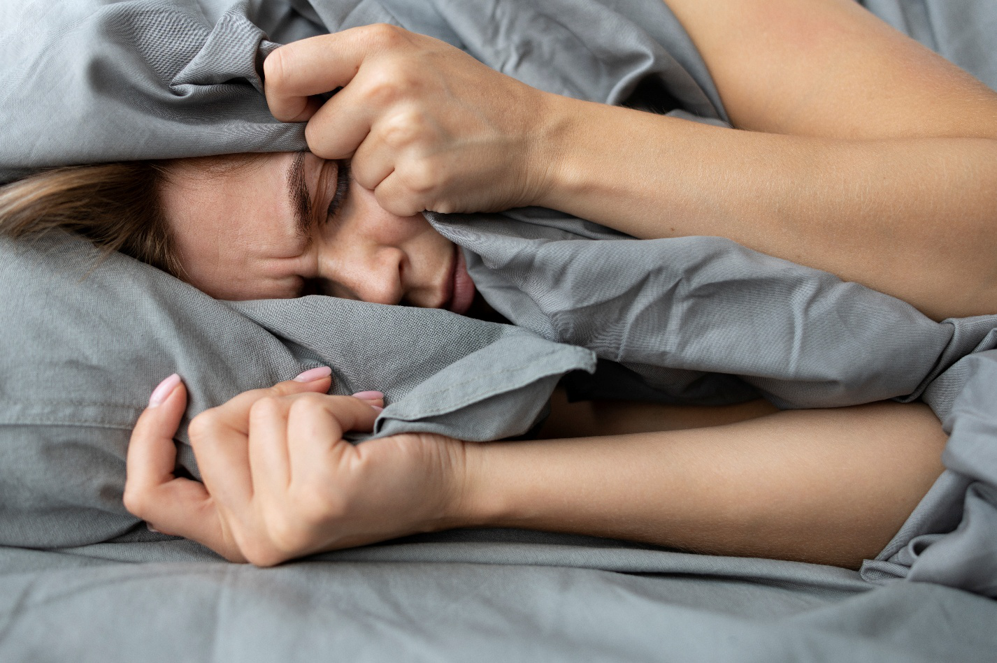 Woman struggling with restless sleep under a blanket, highlighting the impact of poor sleep on health.