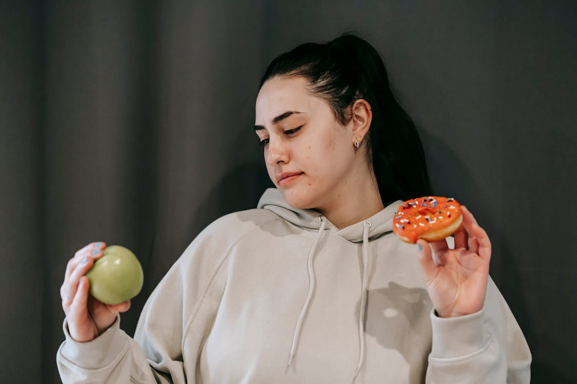 A woman deciding between a healthy apple and a donut for her diet.