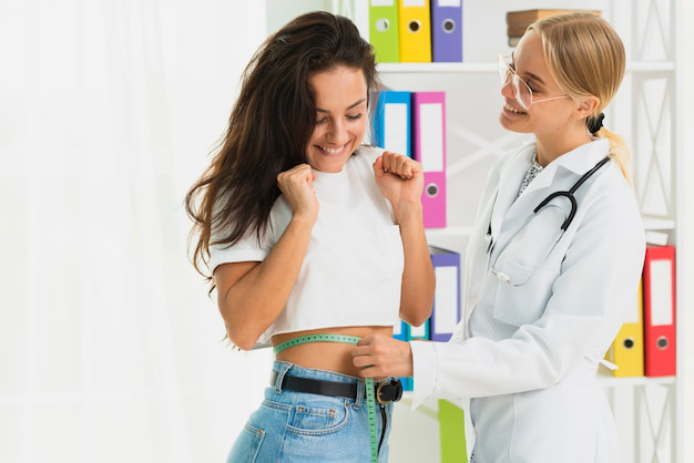 A doctor measuring a smiling patient’s waist.