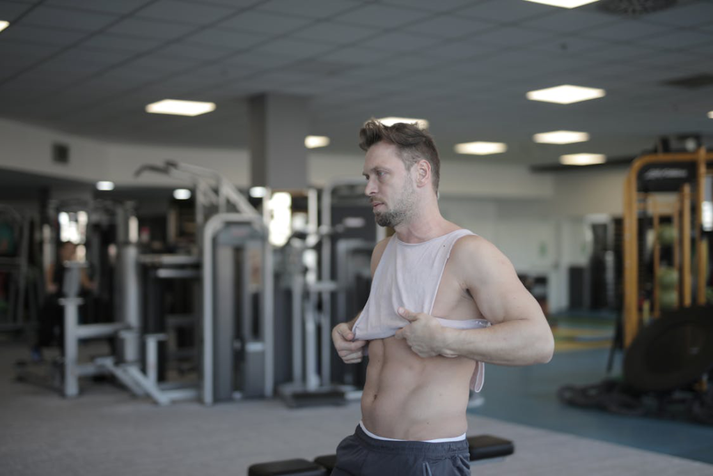 A man in a gym lifting his shirt to check his progress, emphasizing the role of hormones in fitness and body composition.