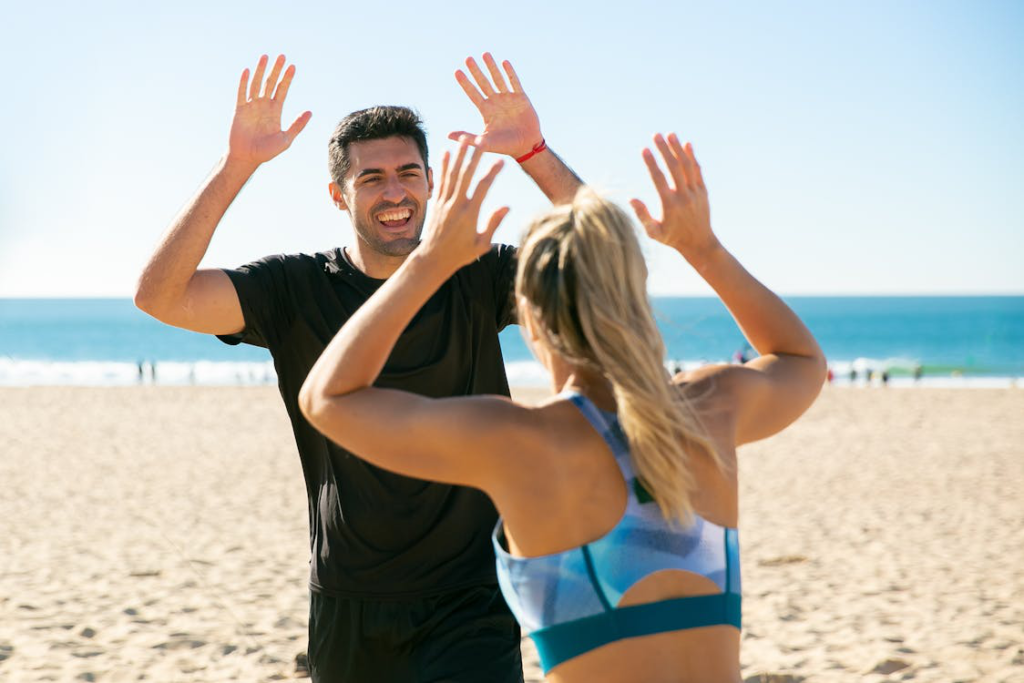 Two people celebrating fitness and vitality with a high-five at the beach.