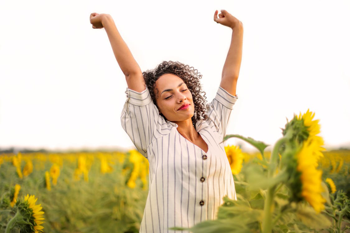 Woman stretching joyfully in a sunflower field, feeling refreshed and revitalized.