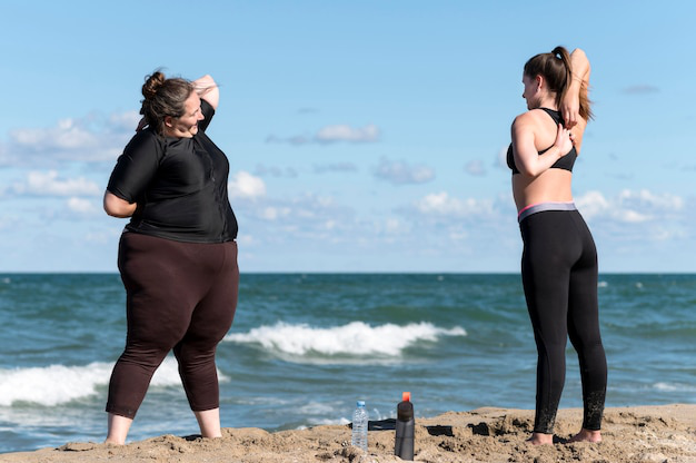  Two women stretching on the beach as part of their weight loss journey.