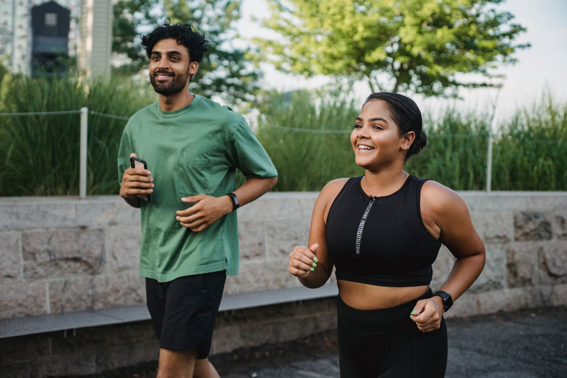 A man and woman jogging outdoors, smiling, and enjoying an active lifestyle.