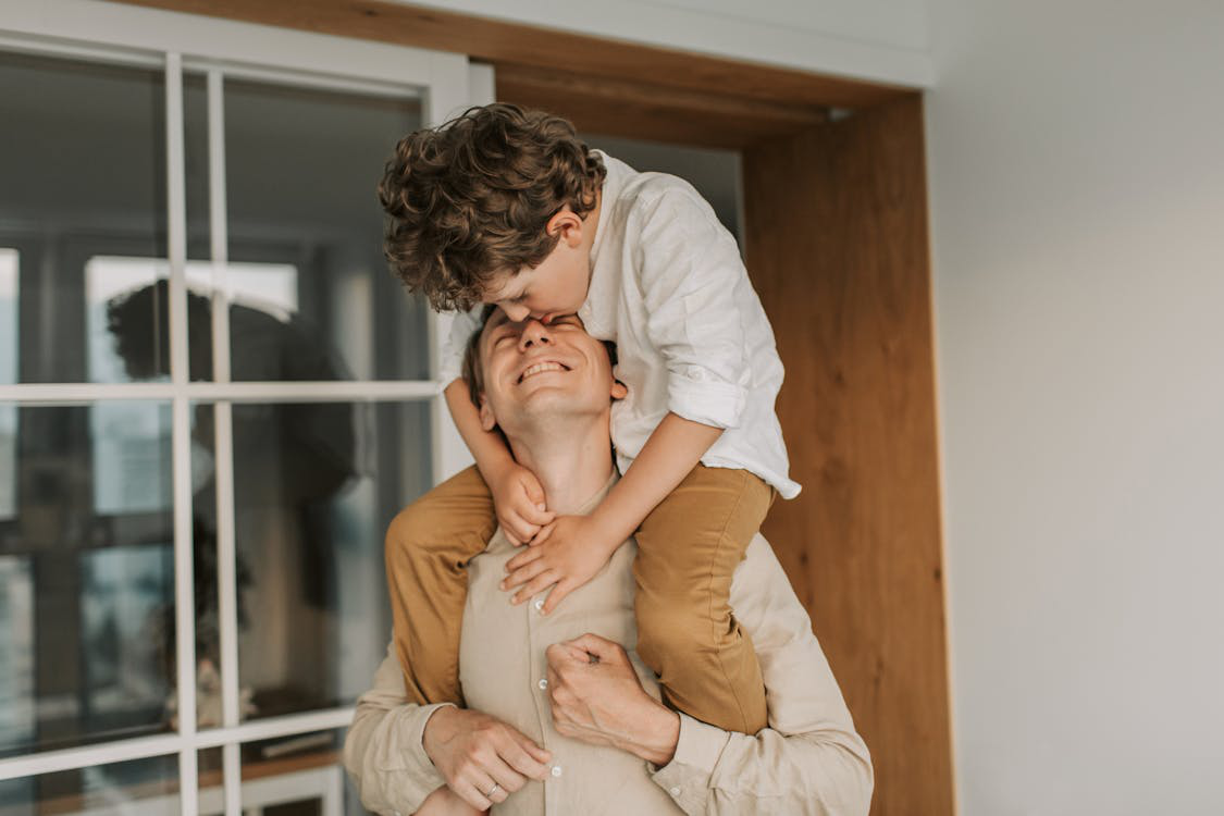 Father enjoying a playful moment with his son on his shoulders at home.