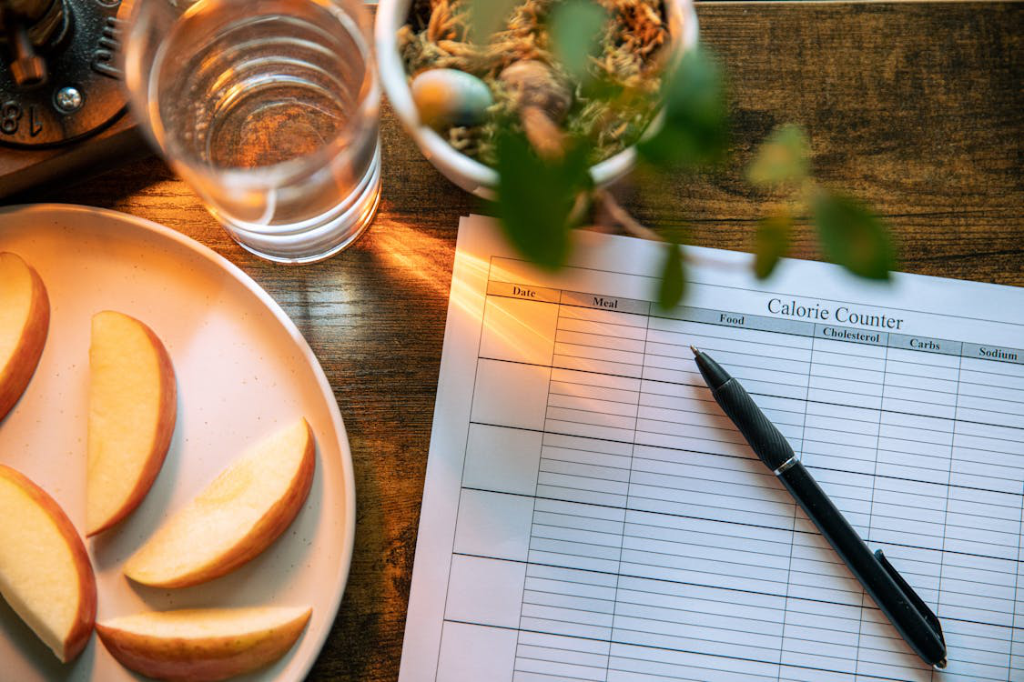 A calorie counter beside sliced apples and water symbolizing healthy diet planning.