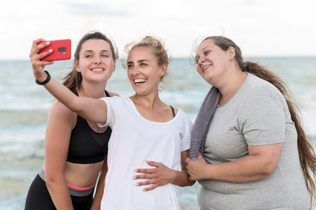 Three women smiling and taking a selfie after a beach workout.