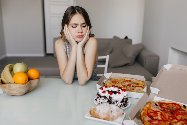 Woman struggling to choose between junk food and healthy fruit