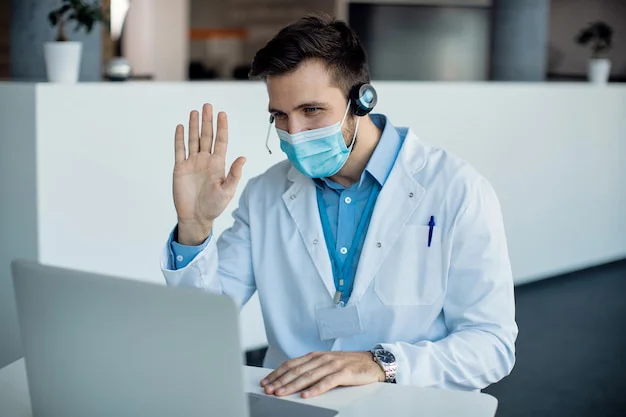 A male doctor waving during a video call on a laptop in a medical clinic.