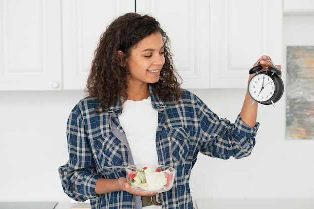 Smiling woman holding a clock and a salad
