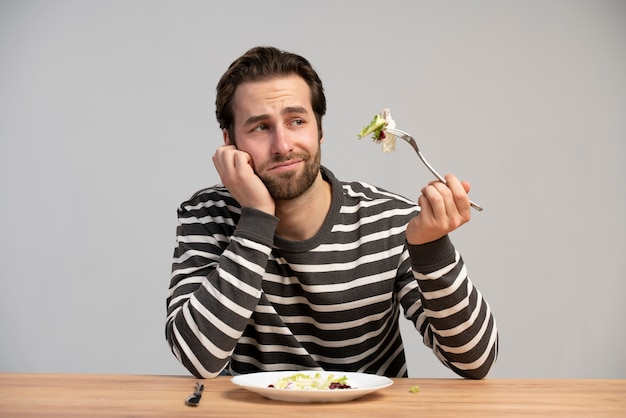  Man looking disappointed while eating salad during weight loss effort