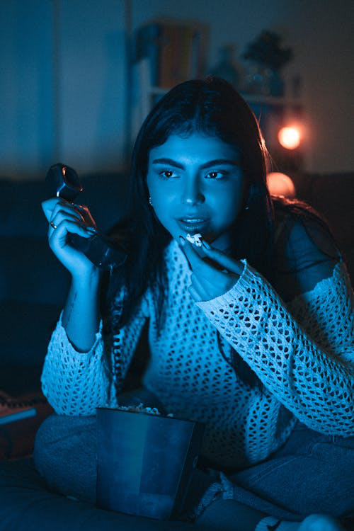 Young woman eating popcorn late at night in front of the TV