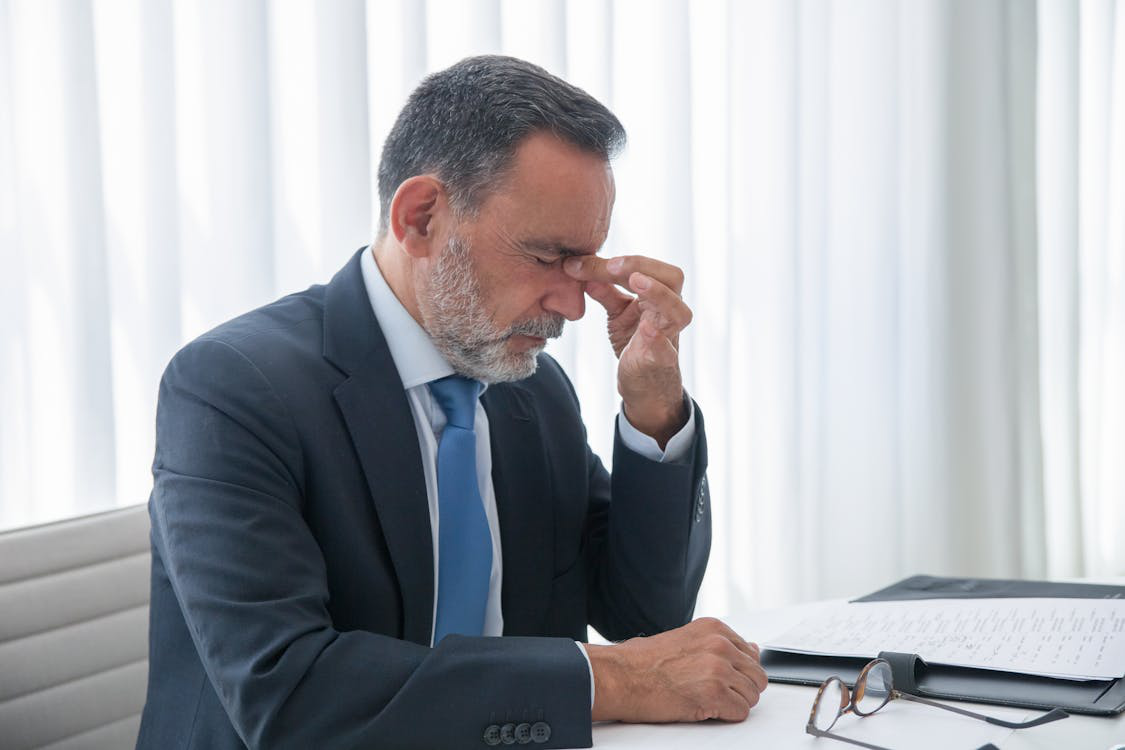 Middle-aged man in business attire showing fatigue, rubbing eyes at his desk