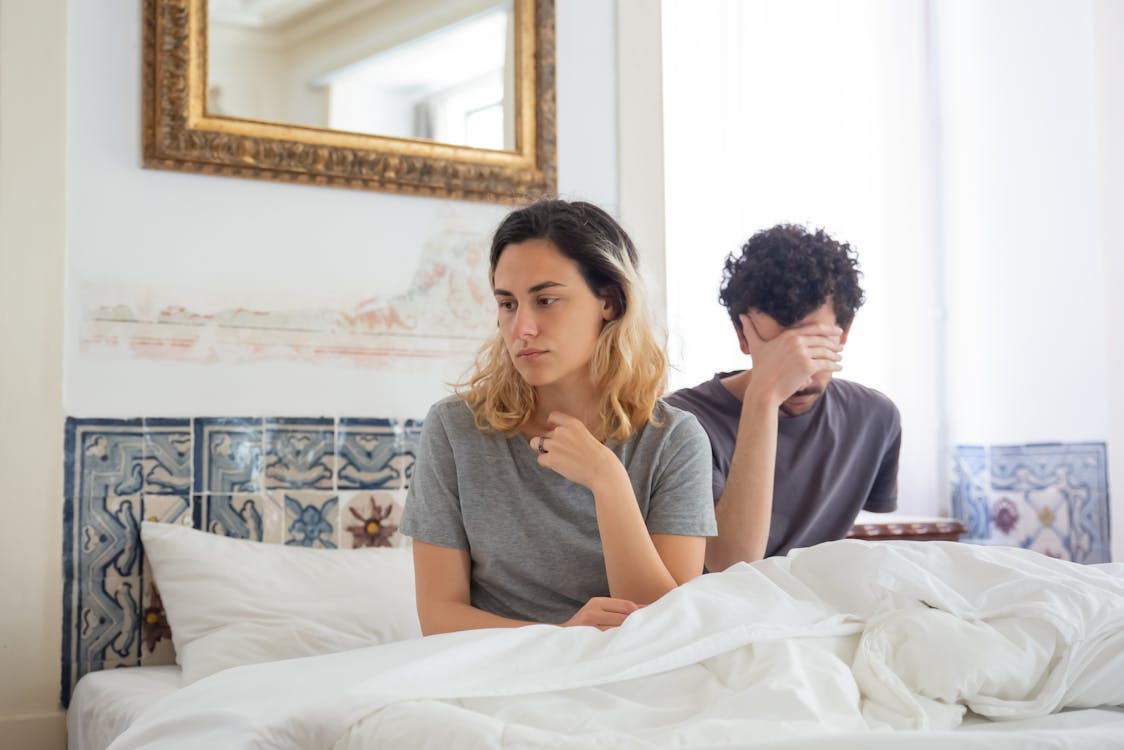 Couple sitting apart in bed, both looking upset and emotionally disconnected