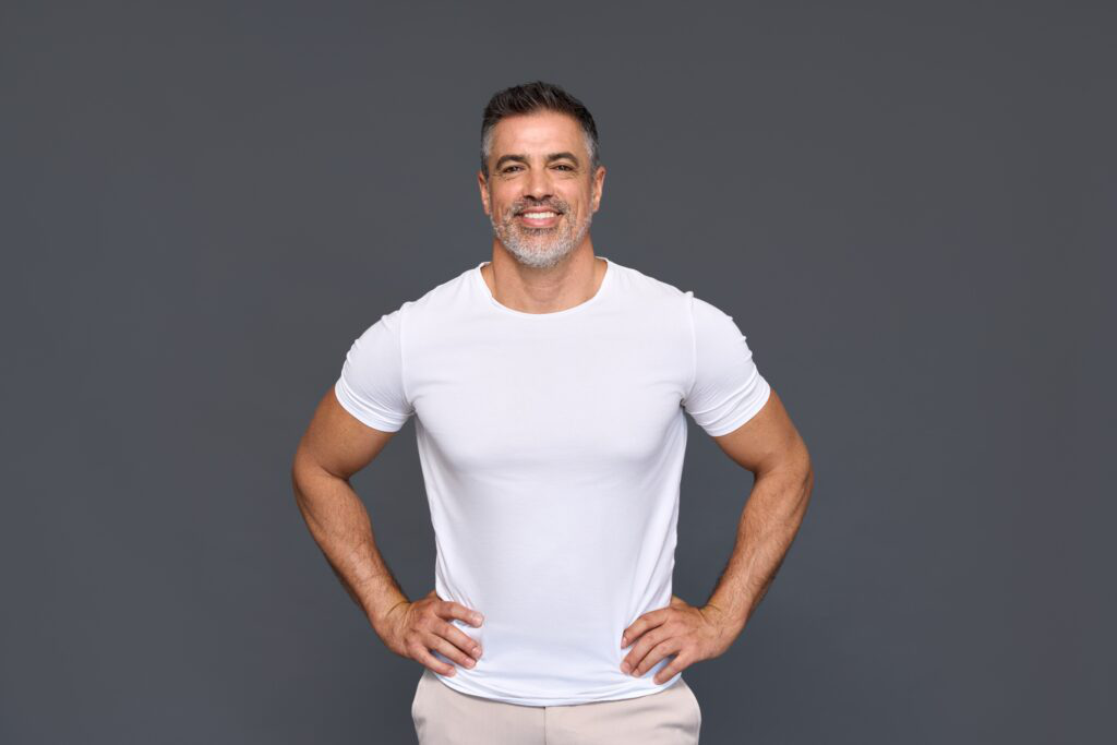 Confident middle-aged man smiling in a white t-shirt with hands on hips