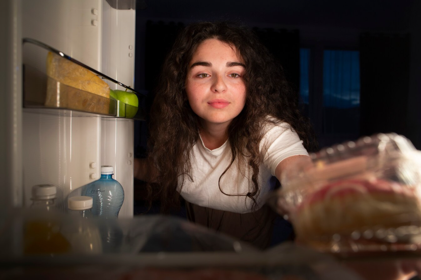 Woman reaching into the fridge late at night with a blank expression