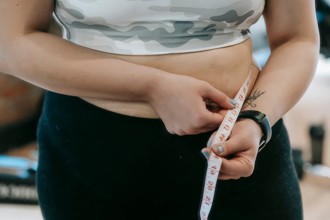 A person measures their waist with a white measuring tape