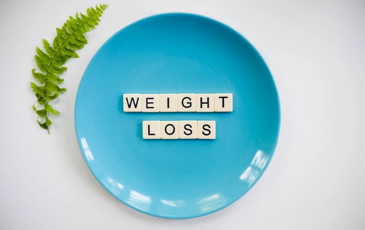 A blue plate has "WEIGHT LOSS" spelled out in letter tiles, with a green fern leaf.