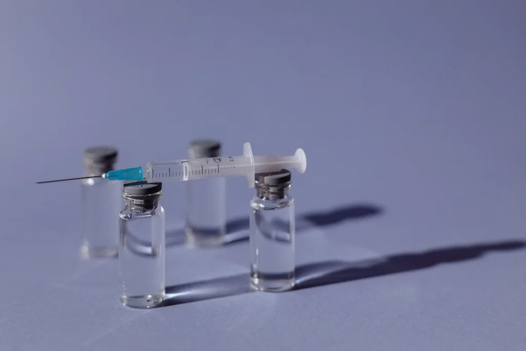 A syringe rests on two clear vials on a purple surface