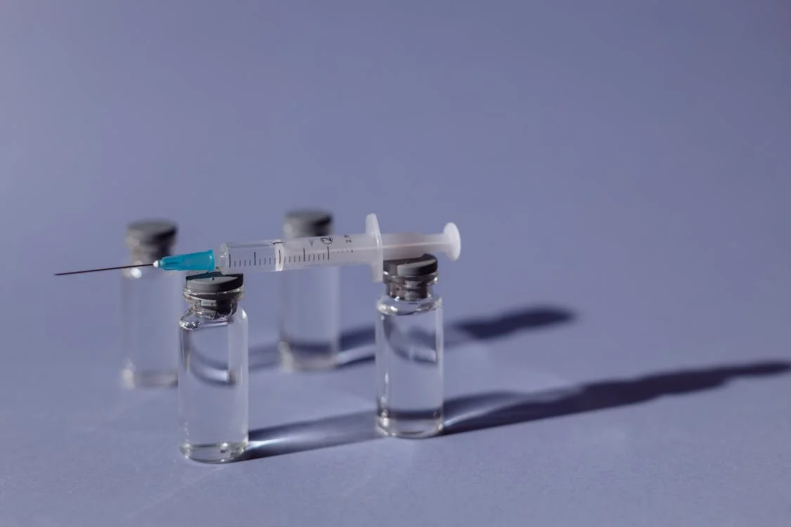 A syringe rests on two clear vials on a purple surface