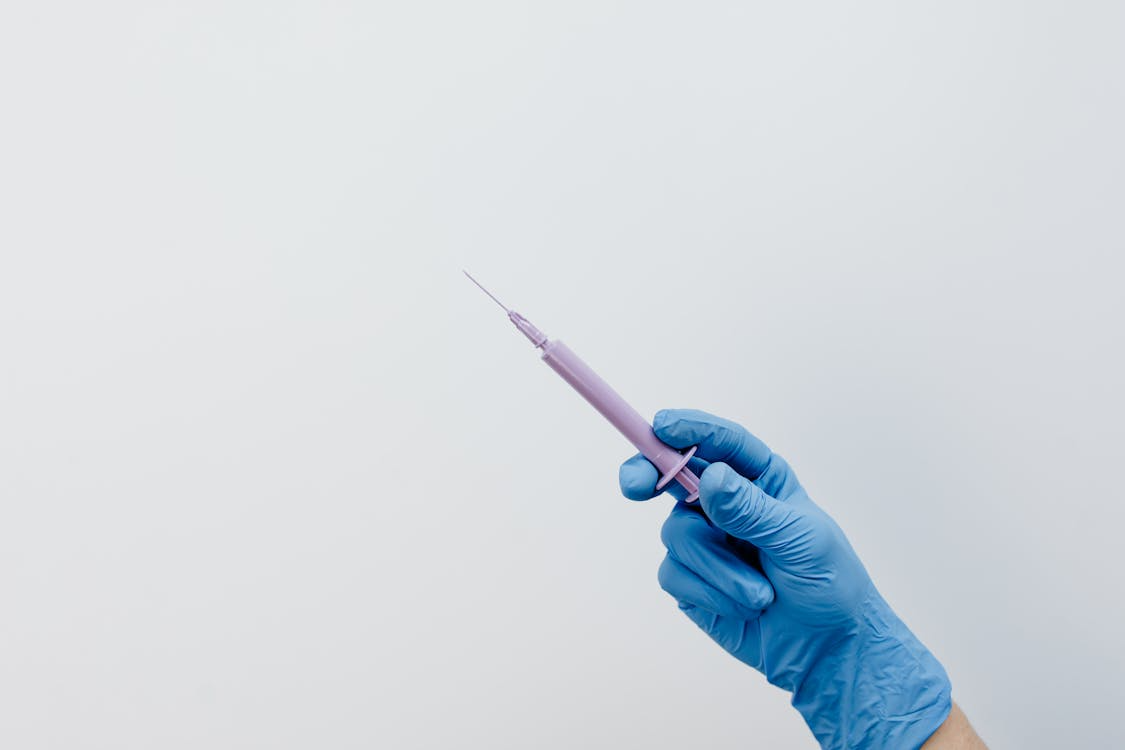 A hand in a medical glove holds a purple syringe with a needle pointed upwards