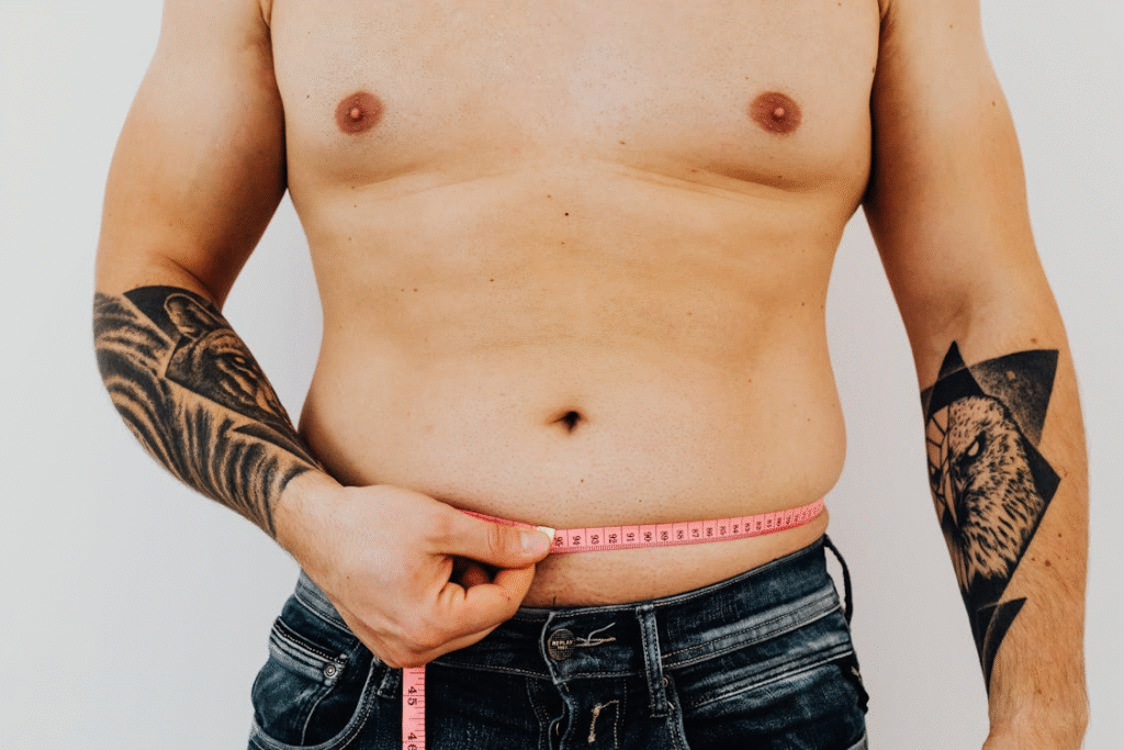 A shirtless person measuring their waist with a pink tape measure