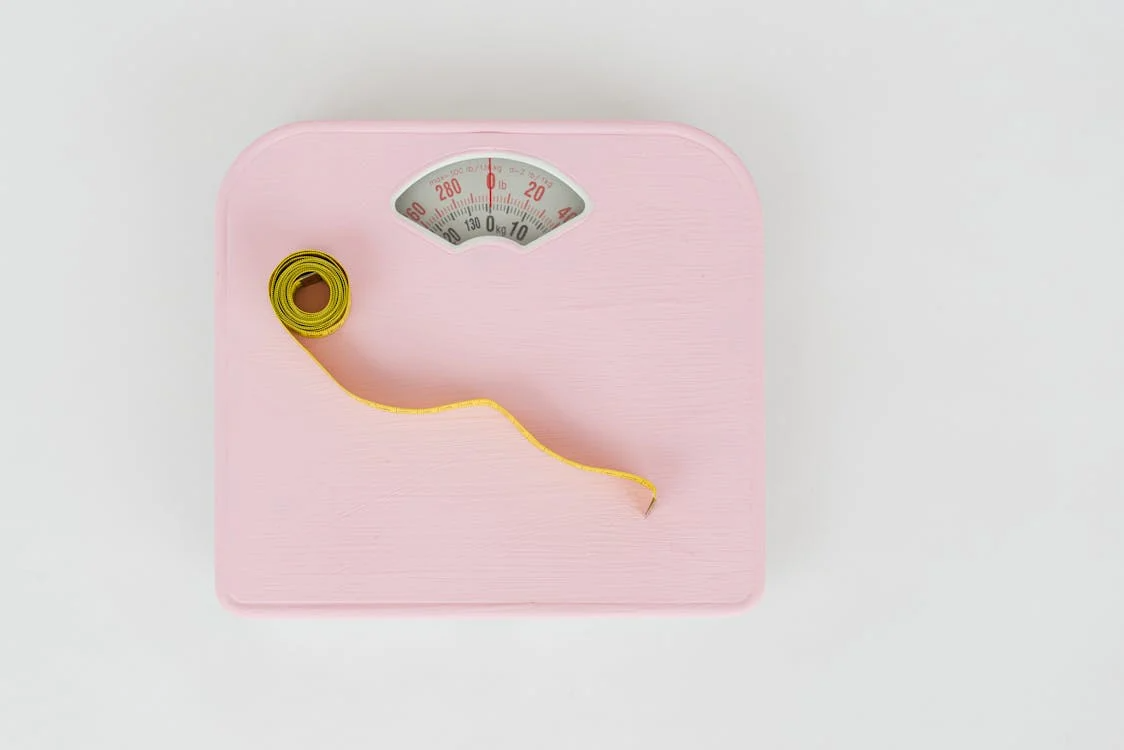 A pink bathroom scale with a yellow measuring tape on it