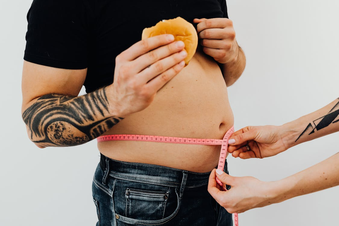 A person having their waist measured while holding a burger.